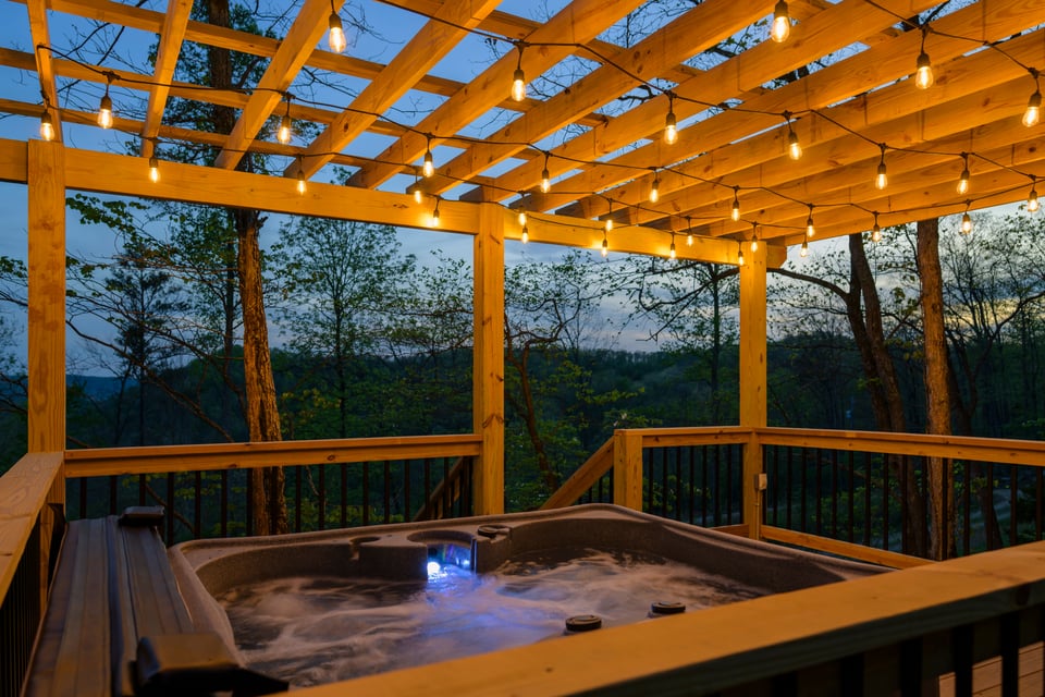 Private hot tub at night with blue LED water, cedar pergola, and mountain ridgeline